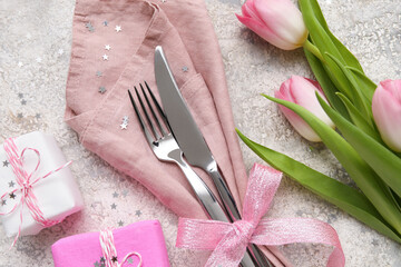 Stylish cutlery with tulip flowers and gift boxes on light grunge background