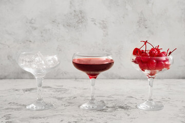 Glass of tasty Manhattan cocktail with ice and cherries on light background