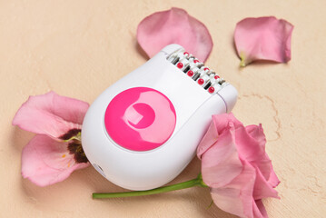 Modern epilator and flower on beige background