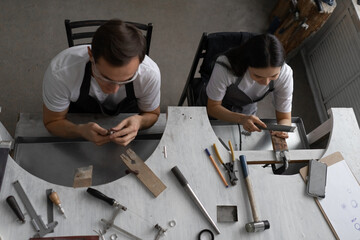 Young couple of jewelers sitting at a workbench. They engaged in preparation of silver rings. Family business, authentic workshop. View from above.