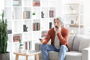 Obraz premium Shocked senior man watching TV on sofa at home