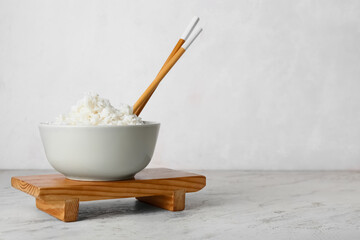 Bowl with tasty boiled rice and chopsticks on light background