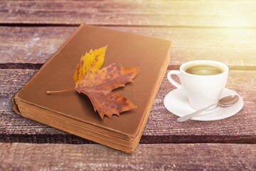 Naklejka na ściany i meble a cup of tea and a book on a wooden surface against the background of fallen leaves, autumn season