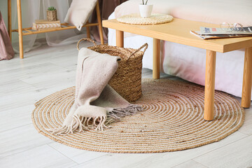 Fototapeta na wymiar Basket with plaid on wicker carpet in bedroom