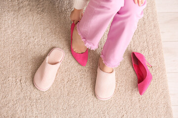 Young woman taking off high heels and putting on soft slippers at home