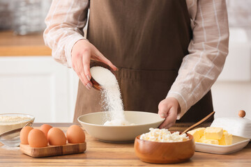 Woman adding sugar into bowl with cottage cheese for preparing pancakes at kitchen table, closeup