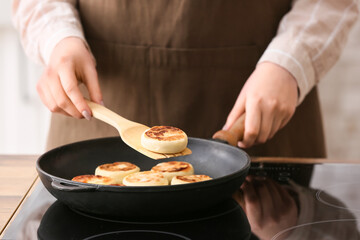 Woman preparing tasty cottage cheese pancakes in kitchen, closeup