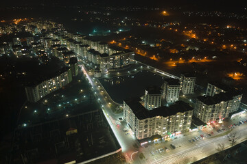 Obraz premium Aerial view of high rise apartment buildings and bright illuminated streets in city residential area at night. Dark urban landscape