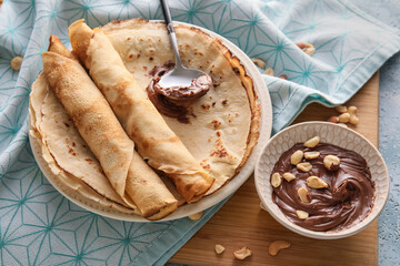 Plate of tasty thin pancakes with chocolate paste and nuts on table