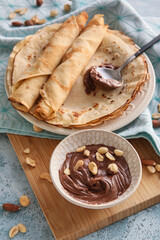 Plate of tasty thin pancakes with chocolate paste and nuts on table