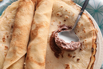 Plate of tasty thin pancakes with chocolate paste on table, closeup