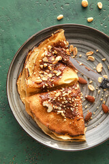 Plate of tasty thin pancakes with chocolate paste and nuts on green background, closeup