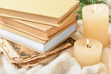 Stack of books with burning candles on plaid, closeup