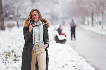 Cheerful young woman smiling in the snow while talking on her cell phone, feeling cheerful and joyful