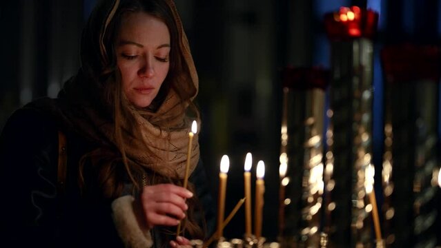 young female parishioner is praying and putting flaming candle in church, portrait
