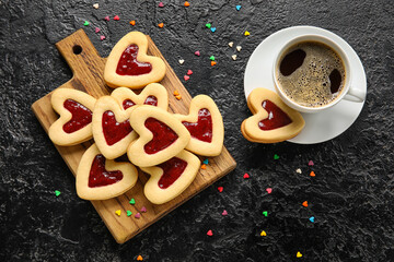 Board with tasty cookies and cup of coffee for Valentine's Day celebration on dark background