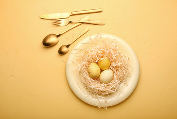 Plate with Easter eggs, decorative shredded paper and cutlery on color background