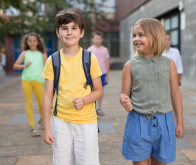 Girl and boy with backpacks are walking along the city street from school