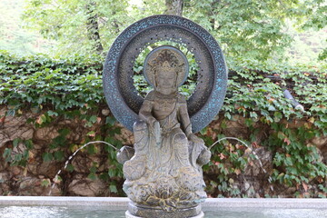 Female Buddhist statue and water fountain. Female deity wears an ornate headdress and encircled by an ornate ring.