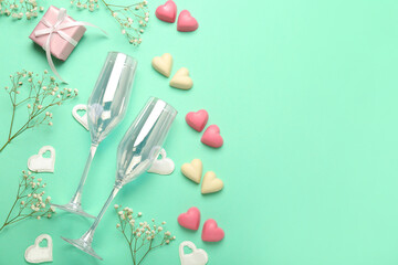Composition with tasty heart-shaped candies, glasses and flowers for Valentine's Day celebration on turquoise background