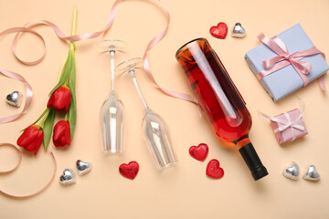 Fototapeta na wymiar Composition with tasty heart-shaped candies, flowers and bottle of wine for Valentine's Day celebration on beige background