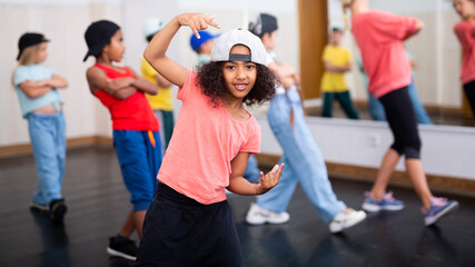 Smiling curly preteen girl dancing hip hop during group dance class for children..