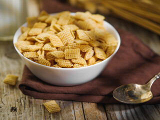 Close-up. Bowl of instant breakfast cereals on a brown napkin and a spoon. In the background is a bunch of cereals. Wooden texture. Supermarket, advertising, banner, poster.