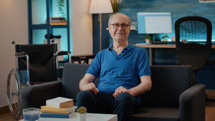Portrait of senior person sitting next to wheelchair at home to help with transportation. Elder man...