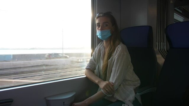 a girl rides in a train in a medical mask looks at the camera shows a sign of peace with her fingers.