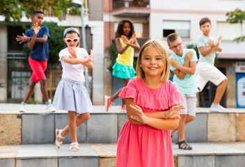 Positive cute girl dancing modern choreography with group of tweenagers on city street on summer...