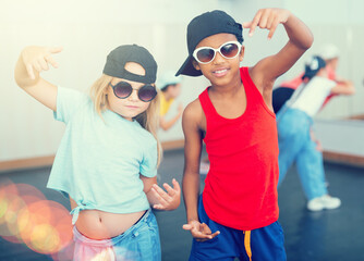 Portrait of boy and girl hip hop dancers posing while friends exercising at dance class