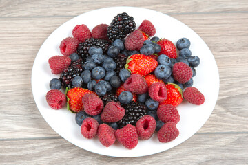 Blackberry, raspberry blueberry and strawberry on a white plate. Vitamins and wholesome foods