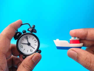 Hand holding clock and toy ships on blue background. Travel concept. - Powered by Adobe