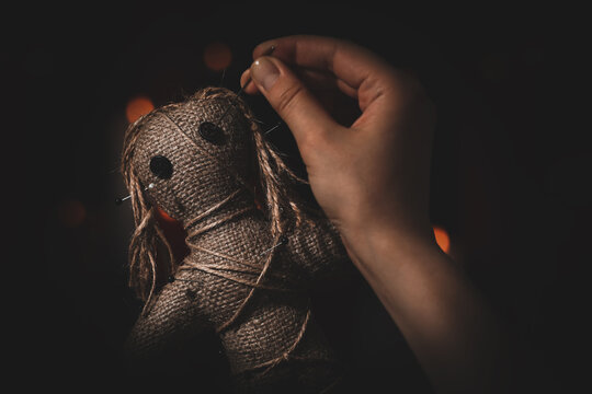 Woman stabbing voodoo doll with pin on dark background, closeup. Curse ceremony