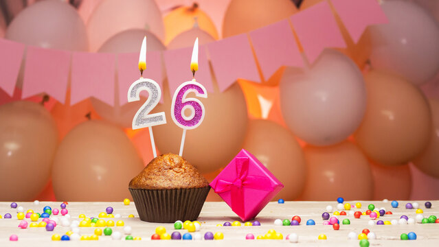 Decorations with balloons and a happy birthday candle with the number 26.  Happy birthday greetings in pink flowers for twenty-six years for a girl,  copy space. Muffin with a burning candle Stock