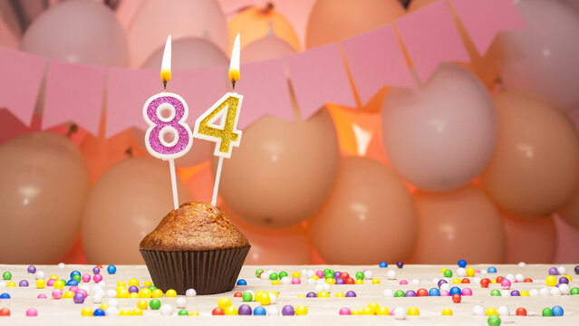 Decorations with balloons and a happy birthday candle with the number 84 for a woman. Happy birthday greetings in pink flowers for eighty-four years old for an elderly woman, copy space. Muffin