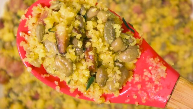 Northeastern Feijao Tropeiro on a spoon, brazilian dish made with cuscuz, string bean, sausage, bacon, chive and curd cheese. Zoom out effect.