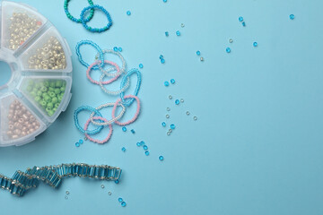 Beautiful handmade beaded jewelry and supplies on light blue background, flat lay. Space for text