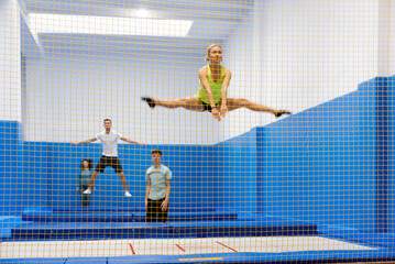 View through yellow safety net of young sporty people exercising jump elements in trampoline center...