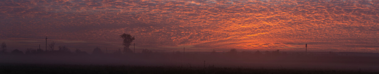 Landscape with bloody sunset. Fog creeps in across the landscape of the earth. Cirrus cloudscape on blue sky. The evening sunset. Majestic Tragic gloomy sky.