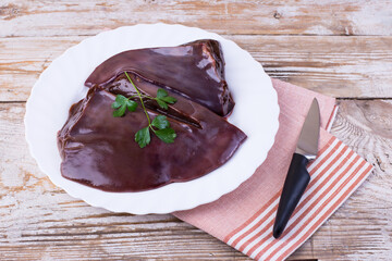 Raw liver on a white plate on a wooden background. Beef liver, top view. Offal in its raw form.