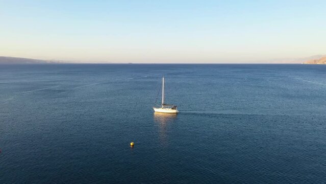 Sailing boat using its engine to sail on a windless day in the gulf of Eilat and navigating next to the buoys. Drone panning shot