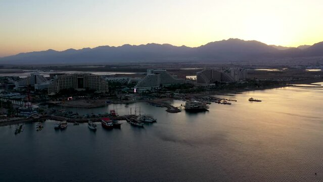 high apartments and hotels at het Gulf of Eilat with an amazing view on the moored boats and high mountains during sunset. Drone panning shot