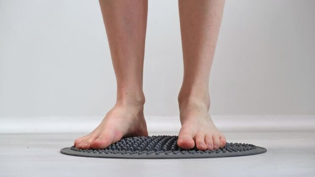 4K. Young girl tramples her feet on an orthopedic massage mat designed for acupressure of the feet. Close-up. Effects on reflexogenic zones. Prevention of diseases. The concept of alternative medicine