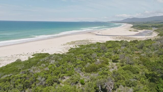 Stunning high angle aerial panoramic drone footage of Lagoons Beach Conservation Area  and Lower Marsh Creek near the village of Scamander on the east coast of Tasmania, Australia on a sunny day.