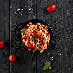 Japanese stir fryed udon noodles in wok. Udon noodle with beef and vegetables on wooden background. Asian noodles on black table with ingredients. Wok menu.