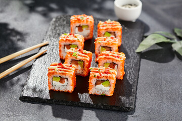 Maki sushi on dark stone table. California maki with tobiko. Sushi roll with cheese,salmon, avocado inside, maguro outside. Style concept japanese menu with black background, leaves and hard shadow.
