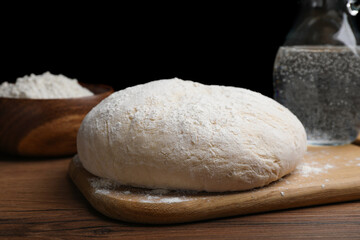 Fototapeta na wymiar Dough on wooden table against black background. Sodawater bread recipe