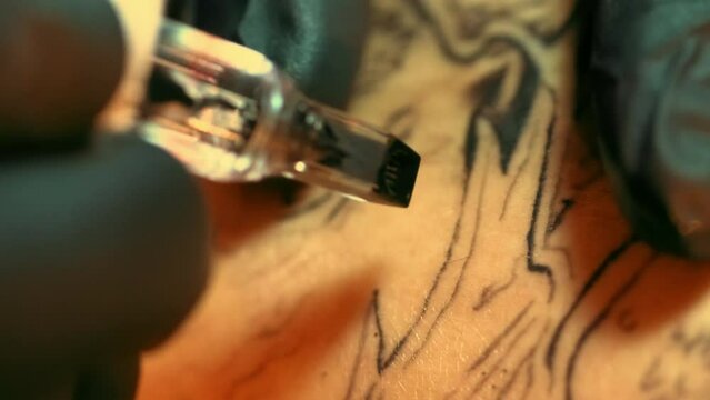 Macro close-up shot of black ink dye pattern filling in clients skin with electric magnum needles bar. Tattoo artists job with customer. Close filming of tattooist working with loading drawing outline