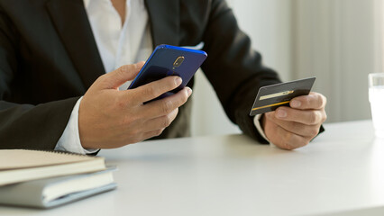 male hand holding credit card and using smartphone online shopping concept Businessman checking account balance Use an online banking app on your mobile phone.